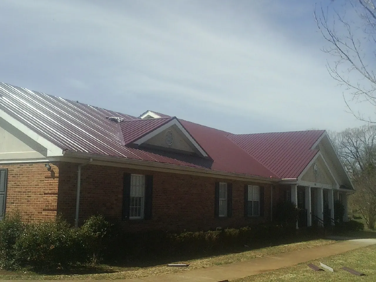 Red metal roof with gabled entries on a long brick building, from a Hail Damage Roof Repair job in Kiel