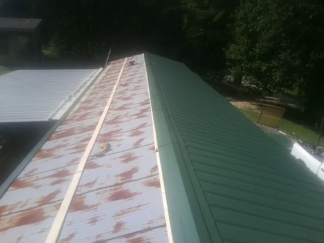 Old rusted panels beside newly installed green metal roofing — Wind Damage Roof Repair by Roofing Brothers in Kiel