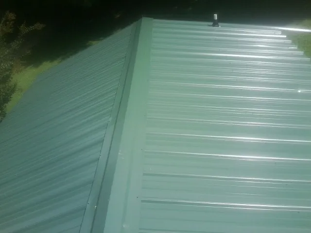New green metal panels meeting at the ridge of a roof — Flat Roof Repair work by our crew in Kiel